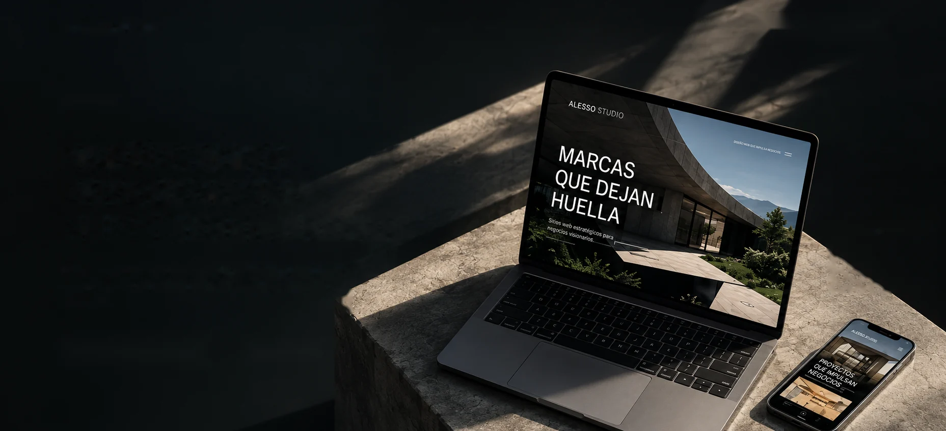 Laptop y celular mostrando sitios web de Alesso Studio sobre un bloque de concreto